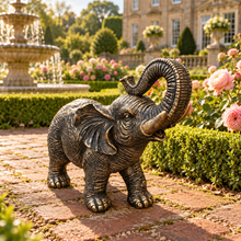 Load image into Gallery viewer, Aged gold polyresin elephant statue with raised trunk in a luxurious garden
