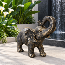 Load image into Gallery viewer, Aged gold polyresin elephant statue with raised trunk in a luxurious garden
