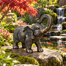 Load image into Gallery viewer, Aged gold polyresin elephant statue with raised trunk in a luxurious garden
