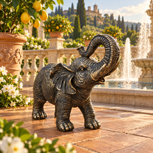 Load image into Gallery viewer, Aged gold polyresin elephant statue with raised trunk in a luxurious garden
