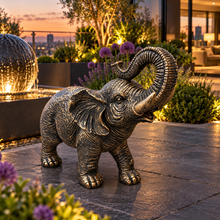 Load image into Gallery viewer, Aged gold polyresin elephant statue with raised trunk in a luxurious garden
