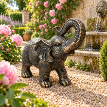 Load image into Gallery viewer, Aged gold polyresin elephant statue with raised trunk in a luxurious garden
