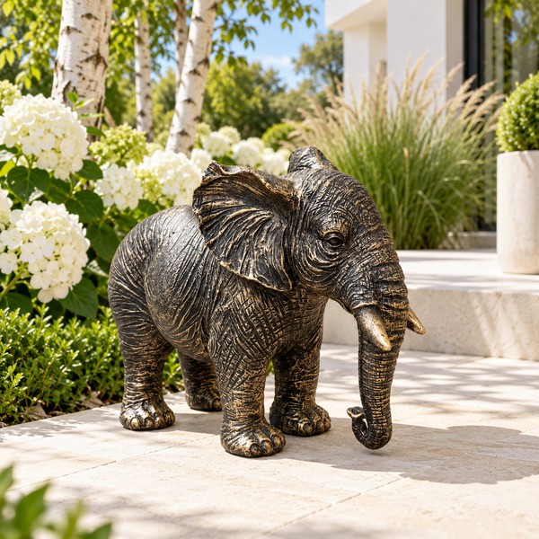 Classic aged gold polyresin elephant with lowered trunk in a luxurious garden
