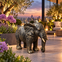 Load image into Gallery viewer, Classic aged gold polyresin elephant with lowered trunk in a luxurious garden
