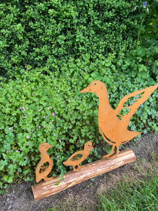Rusty metal duck and two ducklings displayed on a log of wood